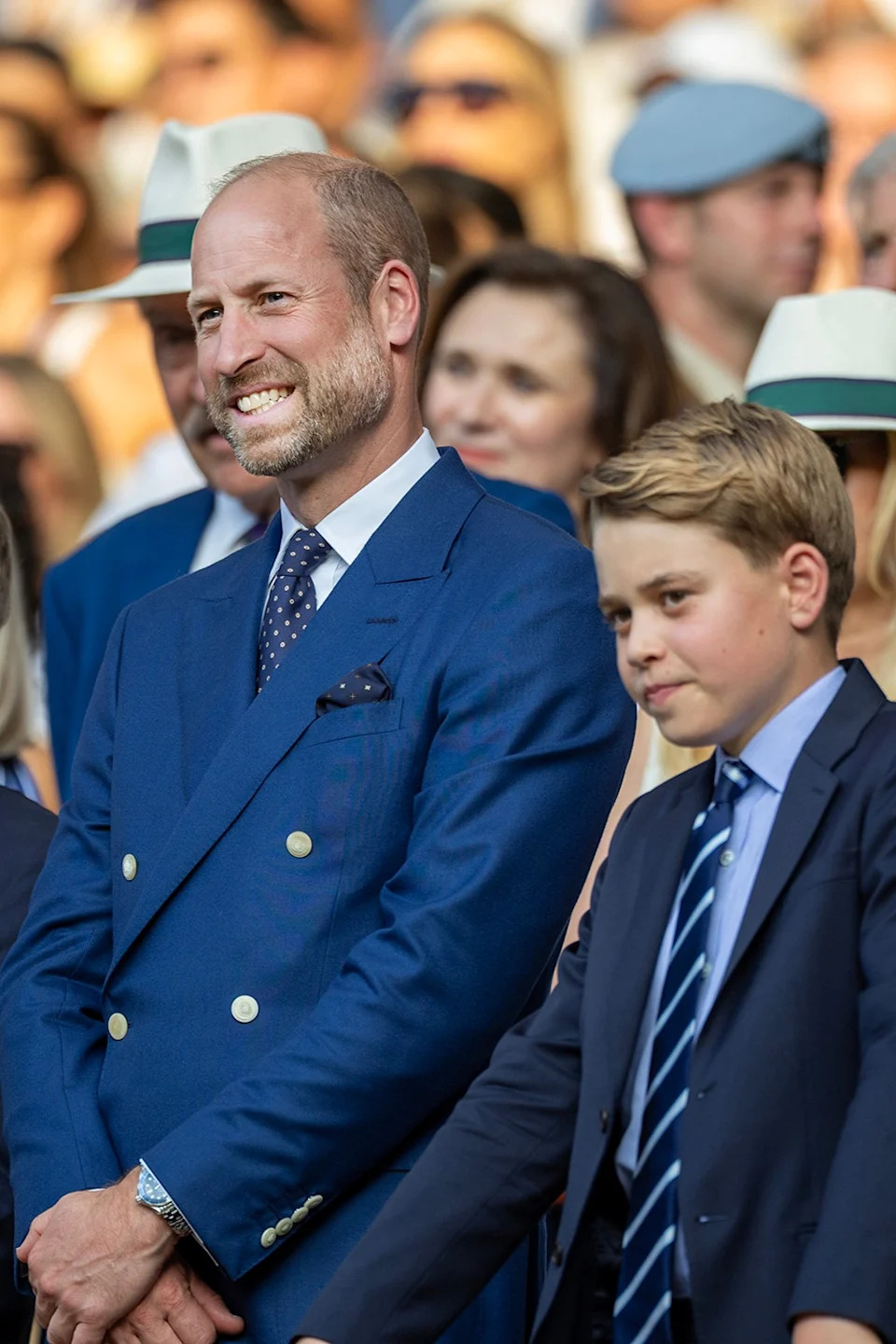Prince William in a blue suit smiling and standing next to his son Prince George.
