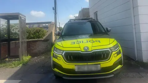 A police car is seen with a blurred out license plate at the scene in Mount Street in Coleraine.  A phonebox and shrubbery can be seen beside the vehicle. 