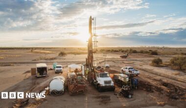 Image of machinery and work trucks on a brown field - the site of Ivanhoe Mining Ltd's Santa Cruz project in Arizona - with the sun setting behind the machinery