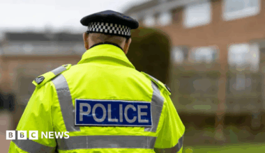 A stock image of a police officer in a high-viz police jacket. The officer's back is to the camera.