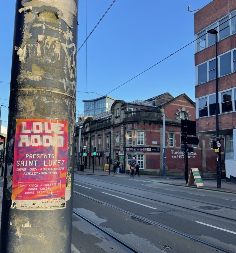 A photo of a flyposter on a lamppost in a city street, advertising a dance night called Love Room