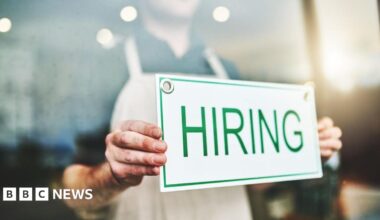 Person holding a sign with the word hiring in green letters on a white background.