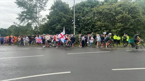 Richard Knights/BBC A large group of people holding the union jack and the St George 's flag. There are police officers at the scene.