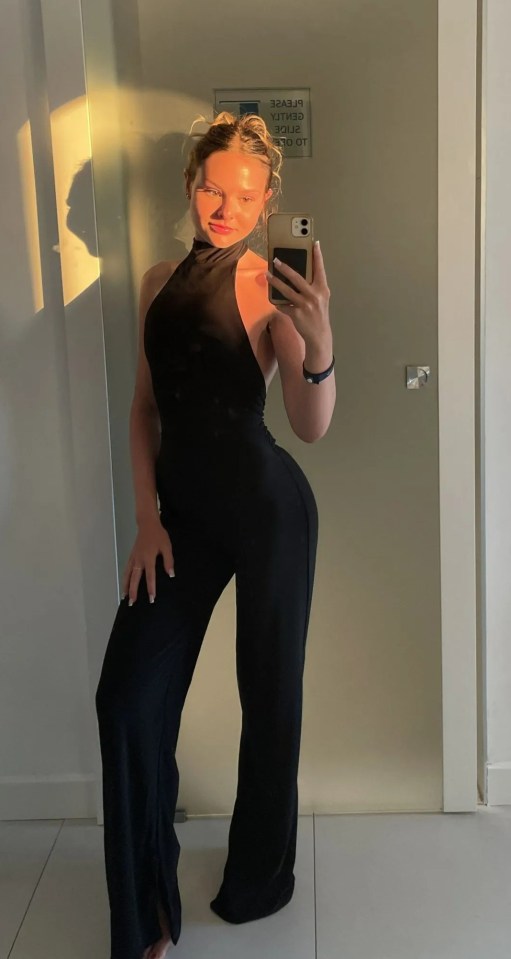 Woman in black jumpsuit taking a selfie.