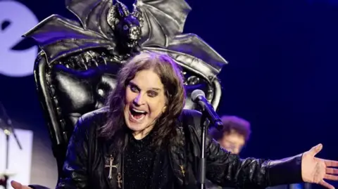 Ross Halfin Ozzy Osbourne, dressed in a black leather jacked sat on a black throne with a microphone in front of him