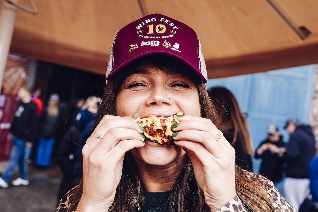a girl in a branded 'Wing Fest' hat taking a bite from a chicken wing