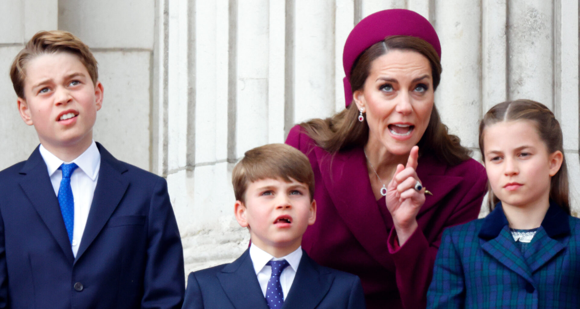 Kate Middleton looks stern while wearing a deep red coat dress and matching hat as she instructs children Prince George, Prince Louis, and Princess Charlotte