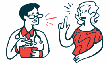 A woman gestures with one hand while speaking with a doctor, who holds a clipboard.
