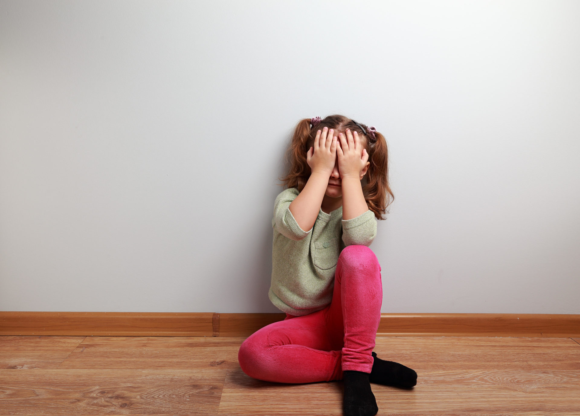 Crying unhappy kid girl sitting on the floor.