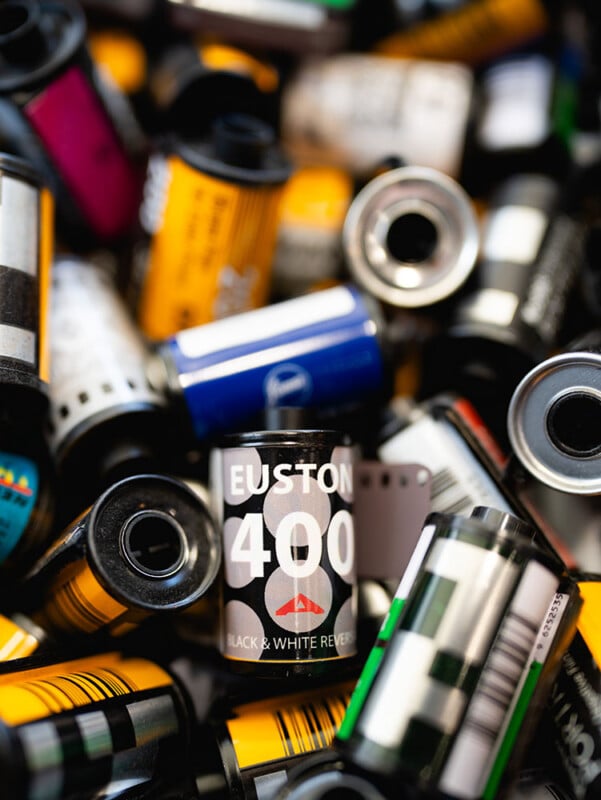 A close-up of several colorful 35mm film canisters, with one black canister labeled "Euston 400 Black & White Reverse" prominently in focus at the center.