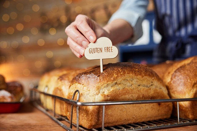 A sales assistant's hand putting a 'Gluten Free' sign in a loaf of bread, with other loaves in the background.