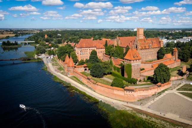 A view of the exterior of Malbork Castle by a river in Malbork, Poland.