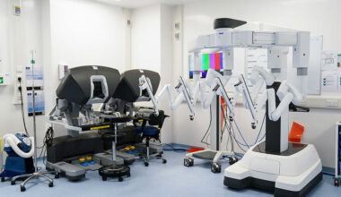 Image of a room in a hospital featuring two surgical robots and two control systems.