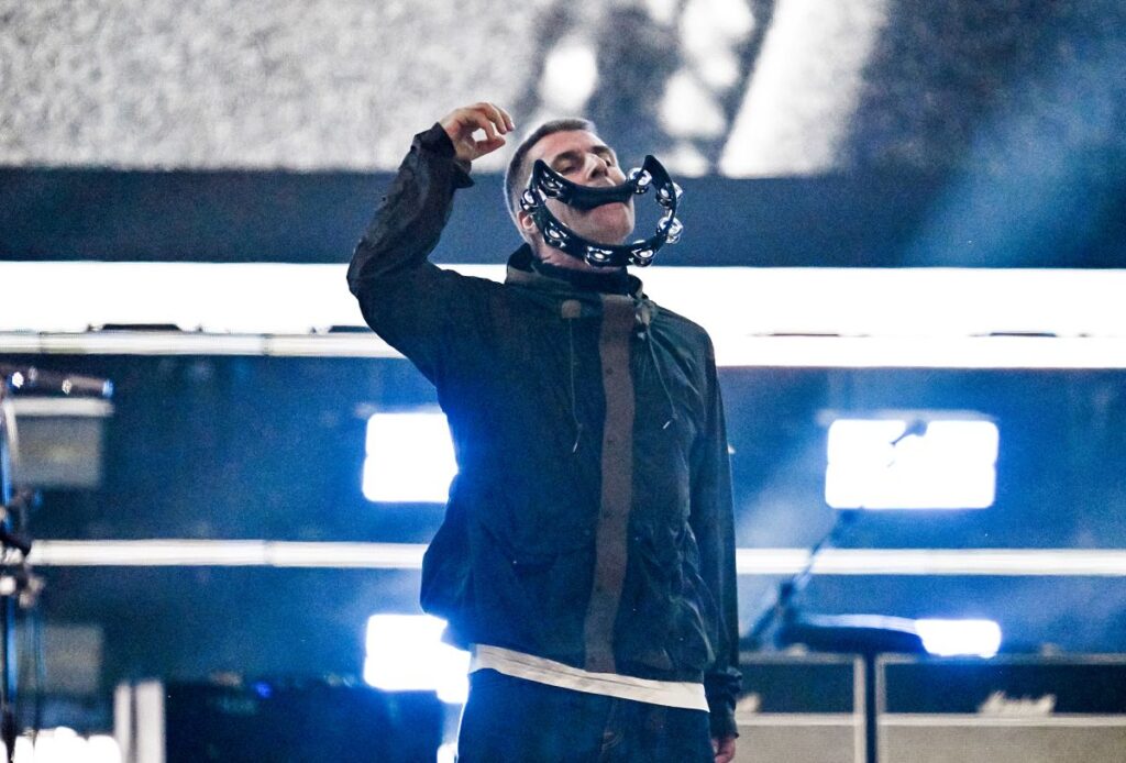 Liam Gallagher holding a tambourine in his mouth at an Oasis show