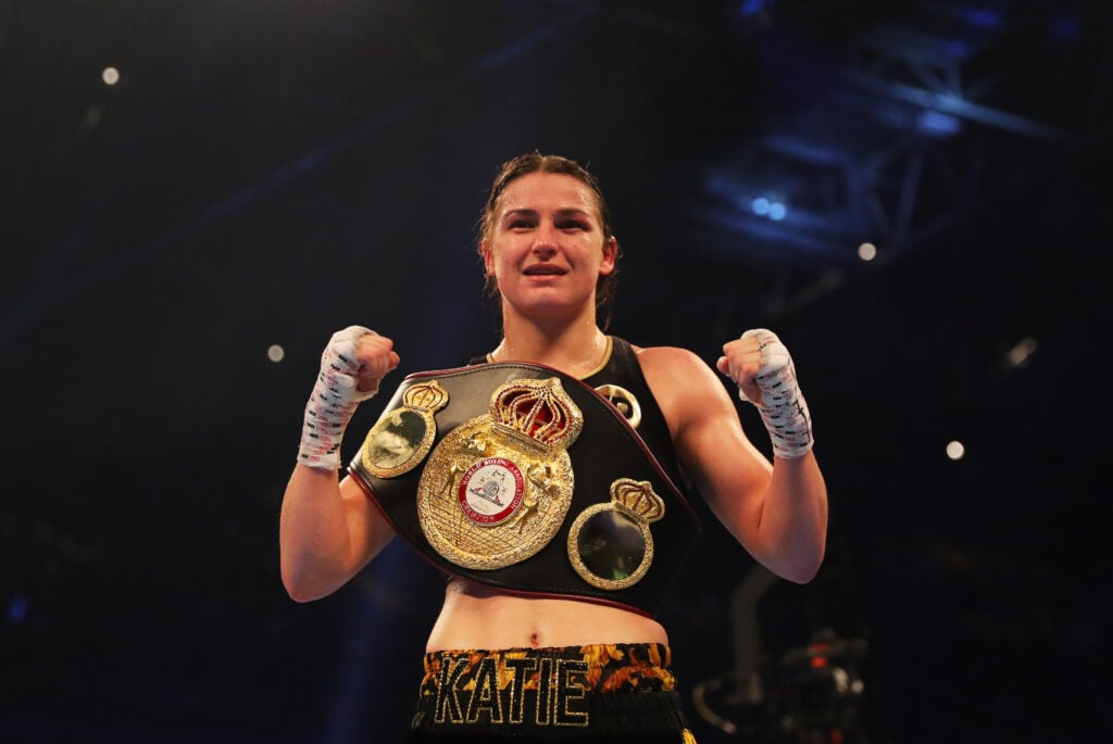 Katie Taylor celebrates her victory over Anahi Sanchez, with her fists up draped in a championship belt