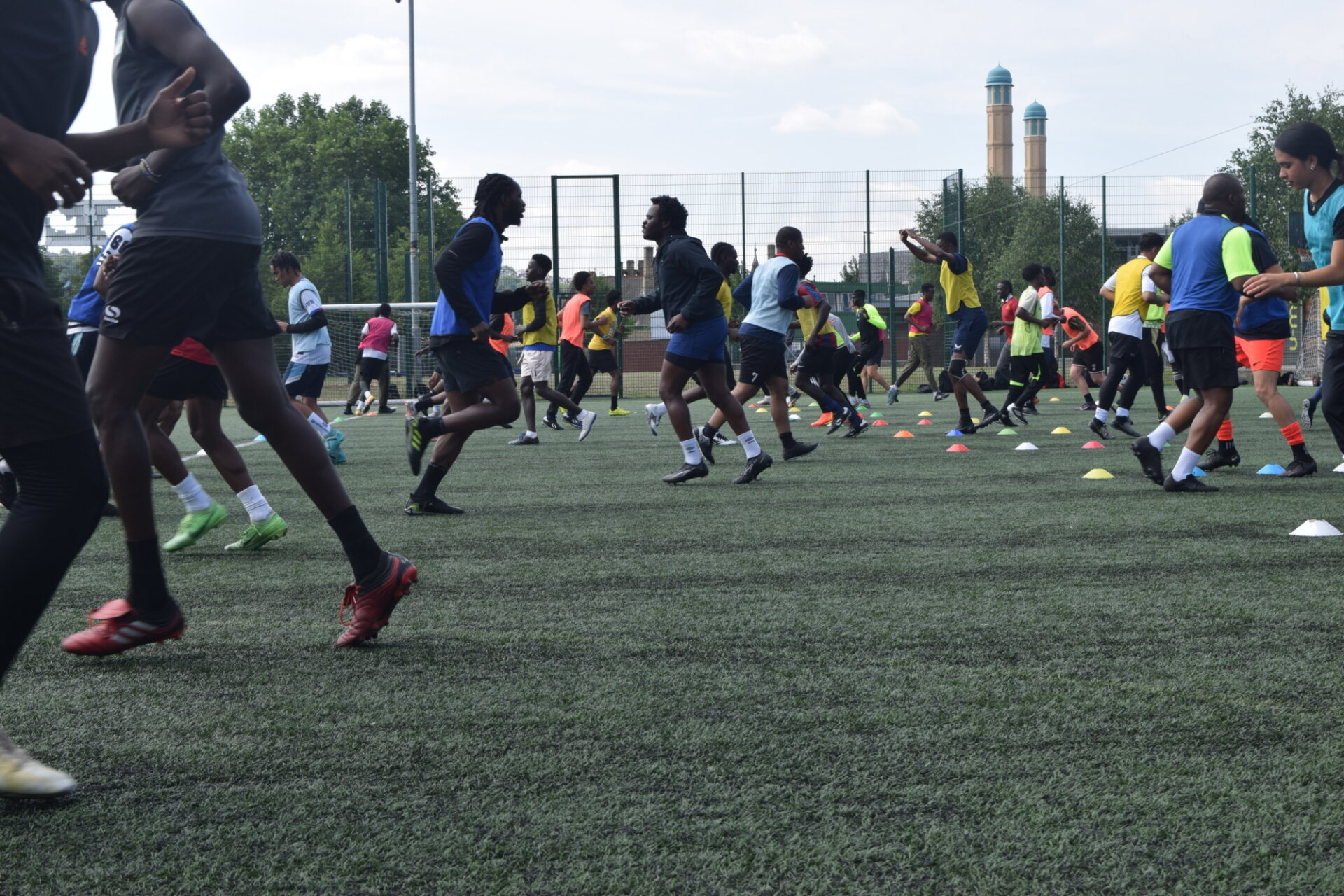 A photo of a big group of men running across the camera on an astroturf field, warming up for football training.