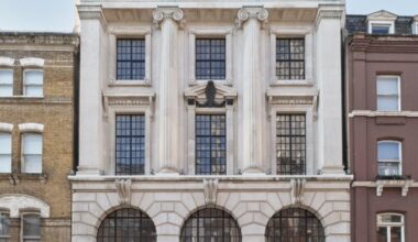 This photo shows a grand, white classical-style building with columns, decorative arches, and large windows. The building