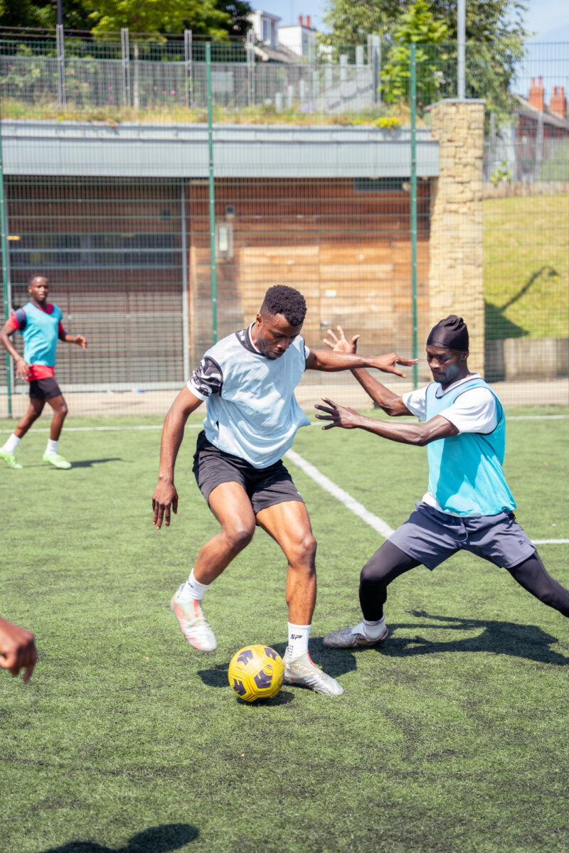 Two young footballers are engaged in what looks like a high energy tackle, with one lunging to try to take the ball from the other.