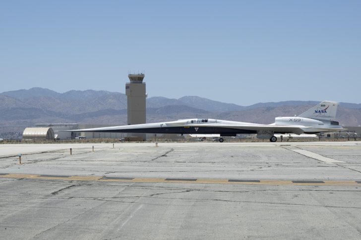 NASA X-59 supersonic aircraft on runway with mountains in the background.