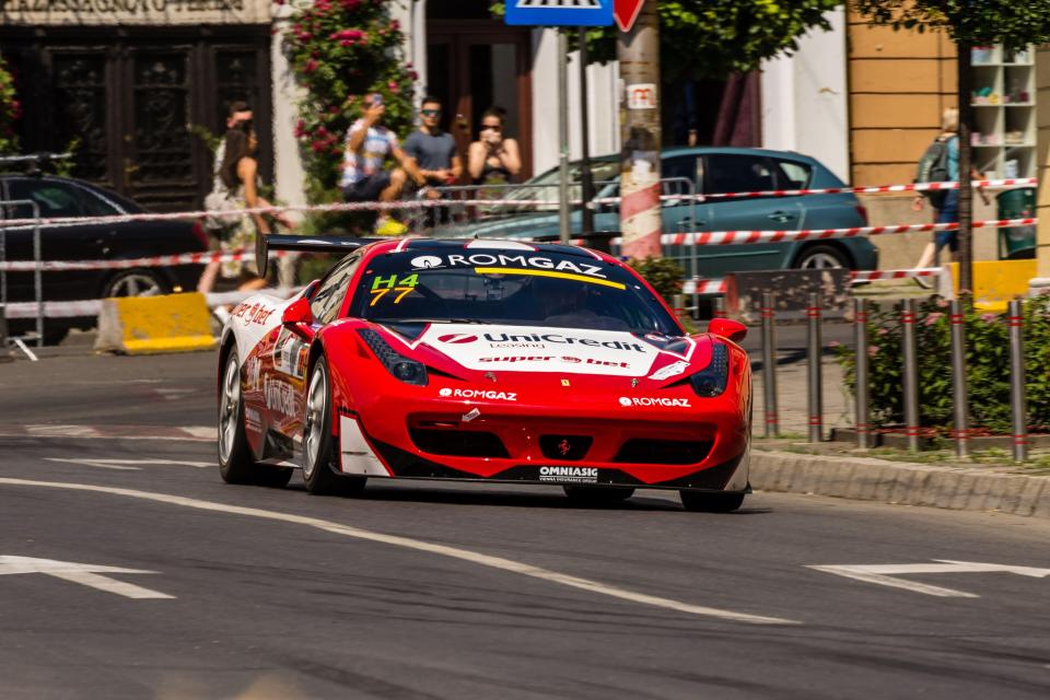 Red Ferrari 458 race car driving on city street.