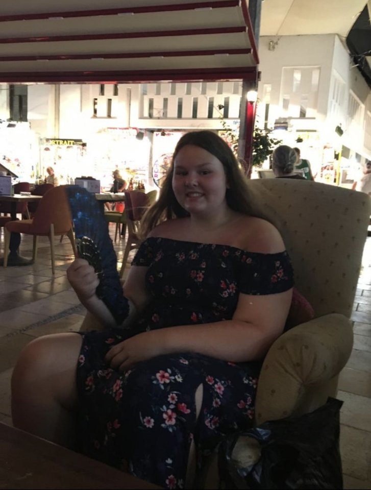 A young woman holding a hand fan sits in a chair.