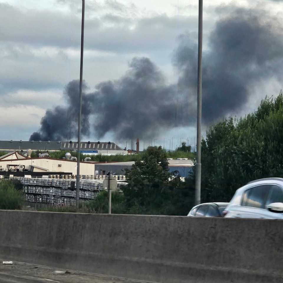 Large plume of black smoke rising above industrial buildings.