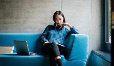 A young woman sitting on a couch looking at a book in a quiet library space.