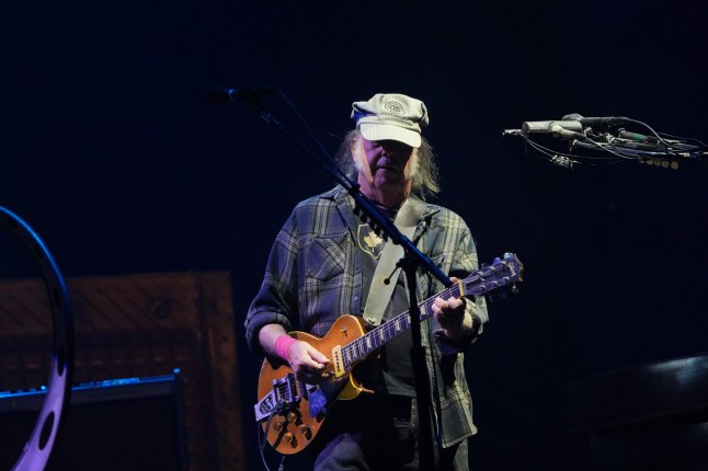 Neil Young performing on the Pyramid Stage with his face half hidden in the shadow of his cap during the 2025 Glastonbury Festival at Worthy Farm