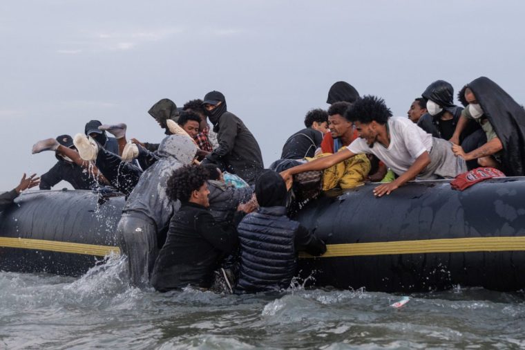 GRAVELINES, FRANCE - JULY 02: Traffickers, (with their faces covered) try to manage the scene using sticks as migrants wade into the water to be collected by a small boat at sunrise on July 02, 2025 in Gravelines, France. Last month, it was reported that French officials were planning changes to policies that govern interceptions at sea, allowing police to intercept small boats within 300 metres of the French shoreline, in a bid to curb migrant crossings of the English Channel. The move, which has not been confirmed, would be welcomed by UK authorities, who see it as a step toward stronger border enforcement. (Photo by Dan Kitwood/Getty Images)