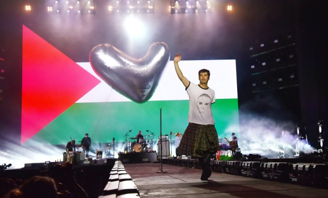 Grian Chatten of Fontaines D.C holds hand in the air in front of Palestine flag