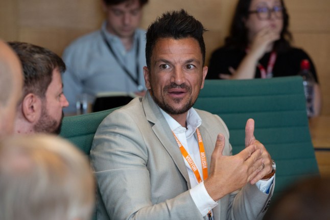 A close up of Peter Andre in a grey suit talking to a man next to him