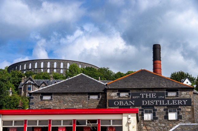 Oban, United Kingdom ??? July 13, 2024: A View of the historic Oban Distillery with McCaig's Tower in the background on a cloudy day in Oban, Scotland