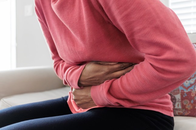 Close-up of unrecognizable black woman sitting on couch holding her abdomen in pain