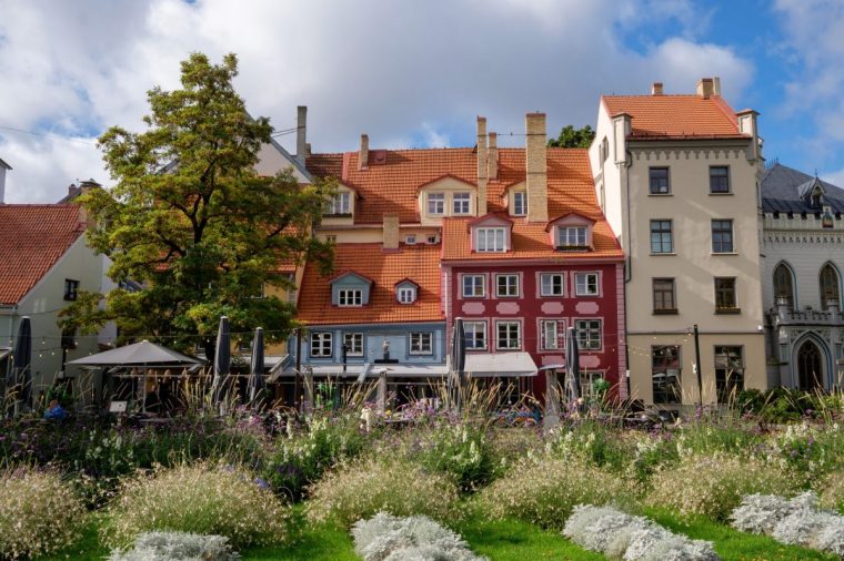 A scenic view of Livu Square in Old Town Riga, Latvia, featuring colorful historic buildings, lush greenery, and outdoor caf????s in a popular tourist destination.