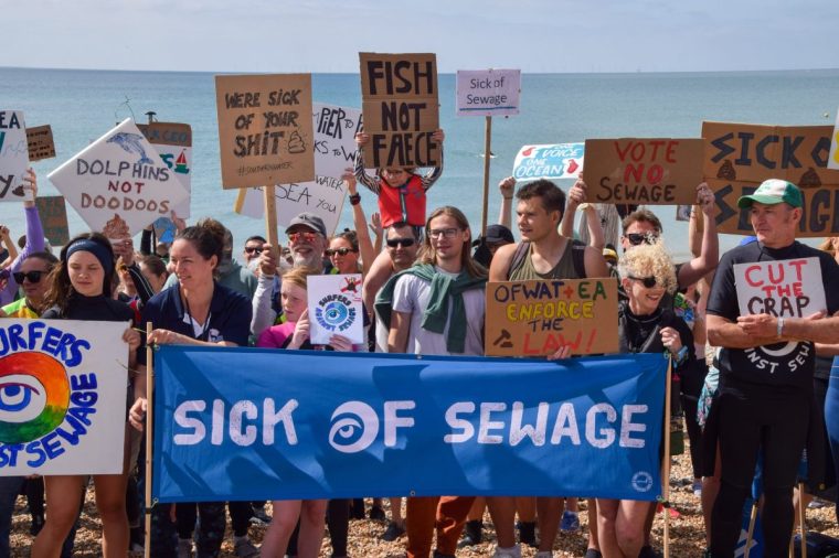 BRIGHTON, UNITED KINGDOM - 2025/05/17: Protesters holding a 'Sick of sewage' banner and placards stand on the beach during the demonstration in Brighton, part of a nationwide Surfers Against Sewage day of action against sewage pollution in British seas, rivers and other waters. (Photo by Vuk Valcic/SOPA Images/LightRocket via Getty Images)