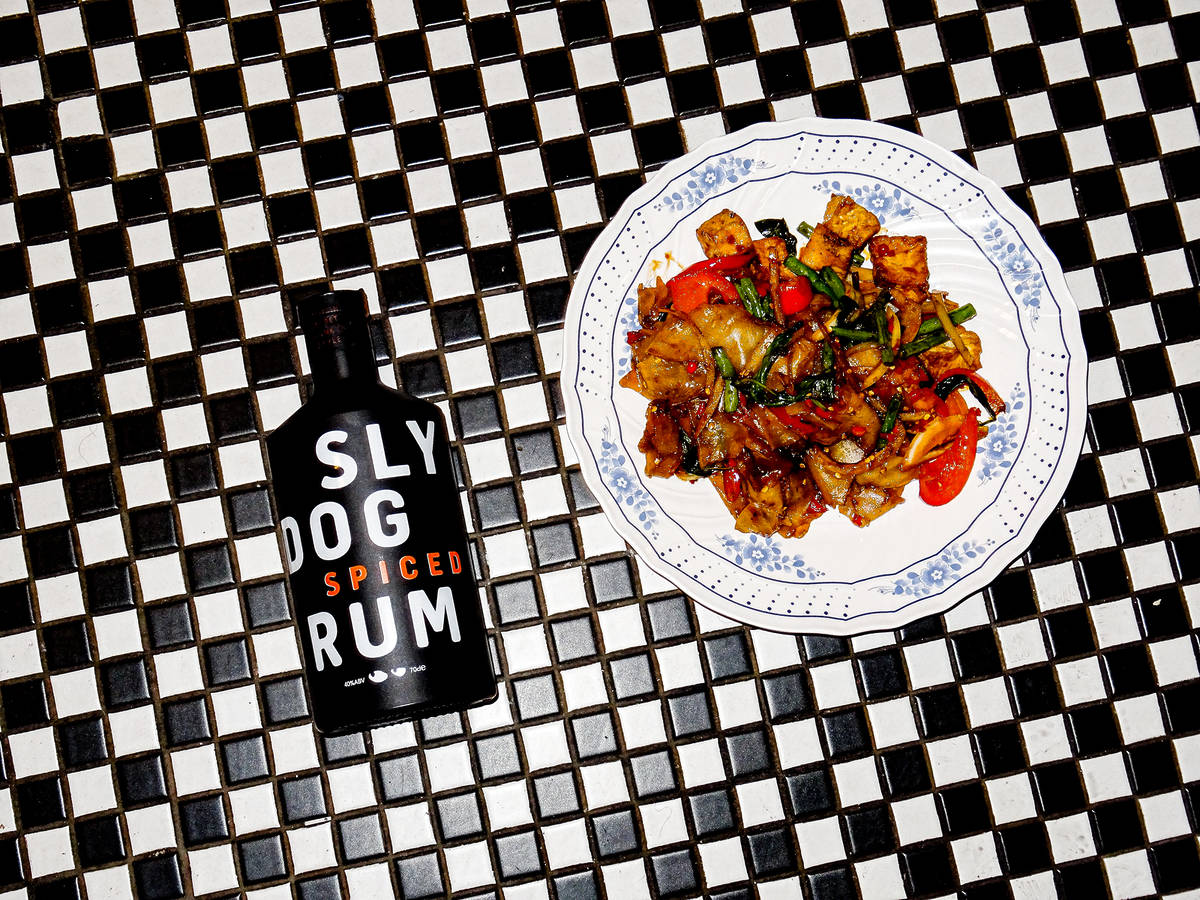a bottle of rum and a plate of noodles presented on a checked black and white tiled surface