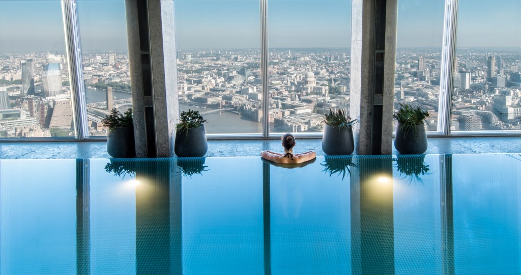 A woman in an indoor rooftop pool looking out a window in London