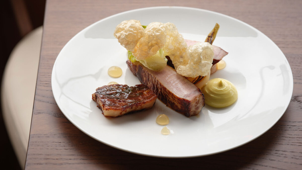 a dish of pork topped with a light but crispy piece of fried pork skin/chicarron