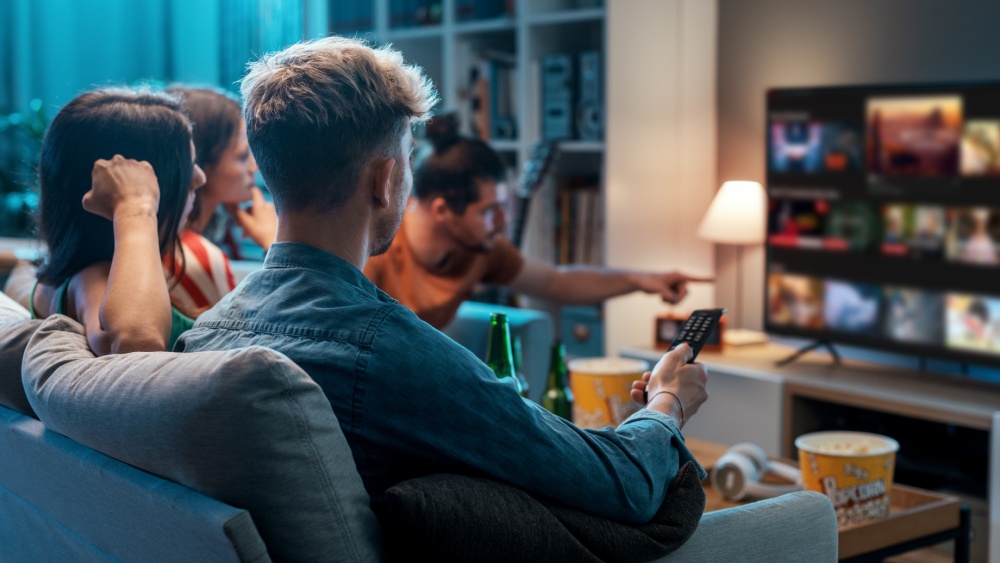 A group of friends sitting on a couch, looking for something to watch on a streaming platform.