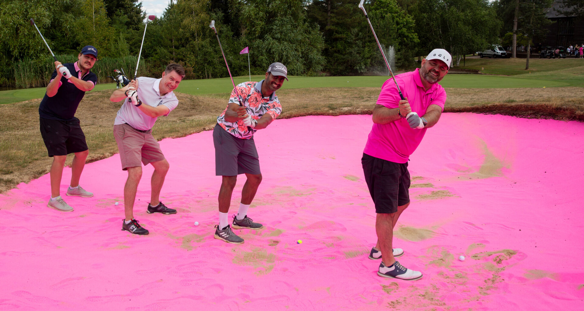 four golfers hitting from pink sand at a charity golf day