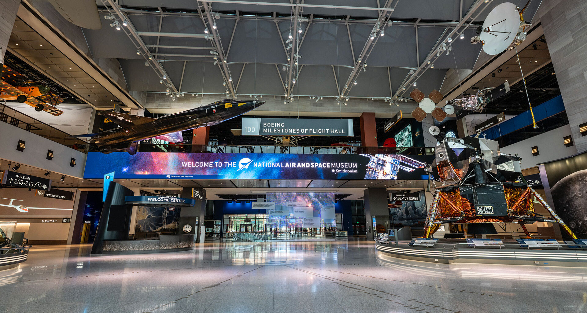 a museum gallery with a wide open space at its center, aircraft suspended from the ceiling and spacecraft standing on the floor