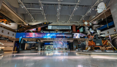 a museum gallery with a wide open space at its center, aircraft suspended from the ceiling and spacecraft standing on the floor
