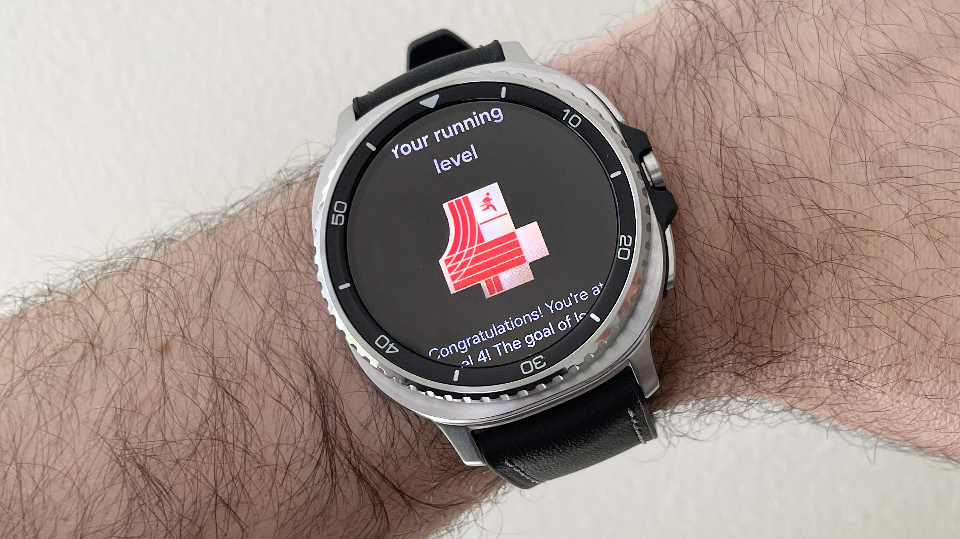 Close-up of the Samsung Galaxy Watch 8 Classic in silver on a black strap showing the Running Coach feature with a score of 