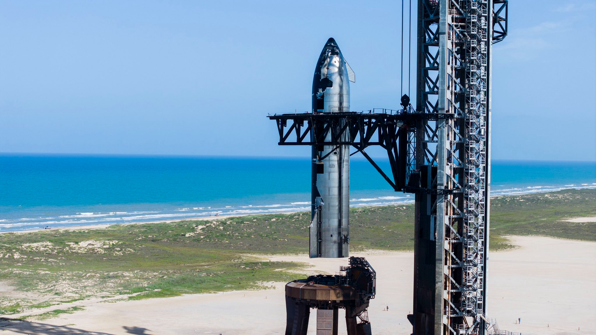 a large silver rocket is lifted onto a launch mount at a seaside pad