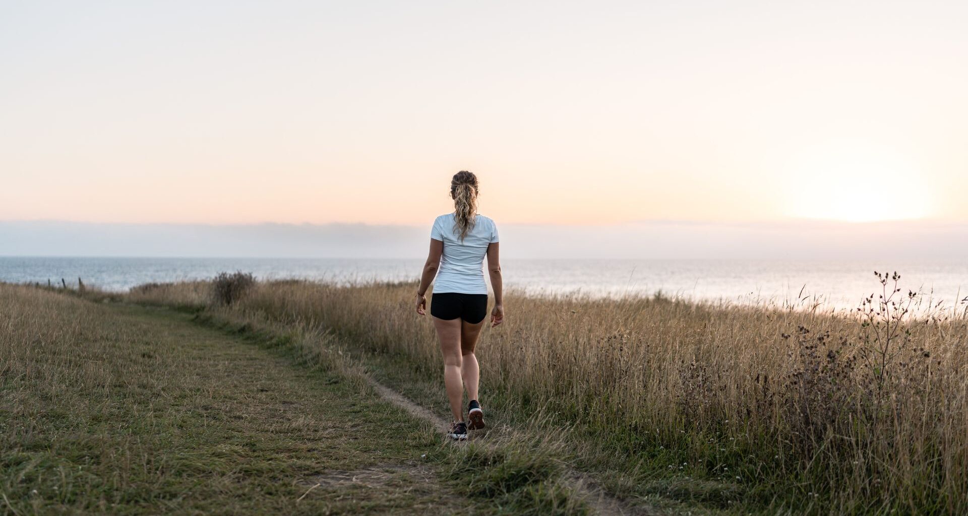 Woman walking along a path by the sea wearing shorts and t-shirt