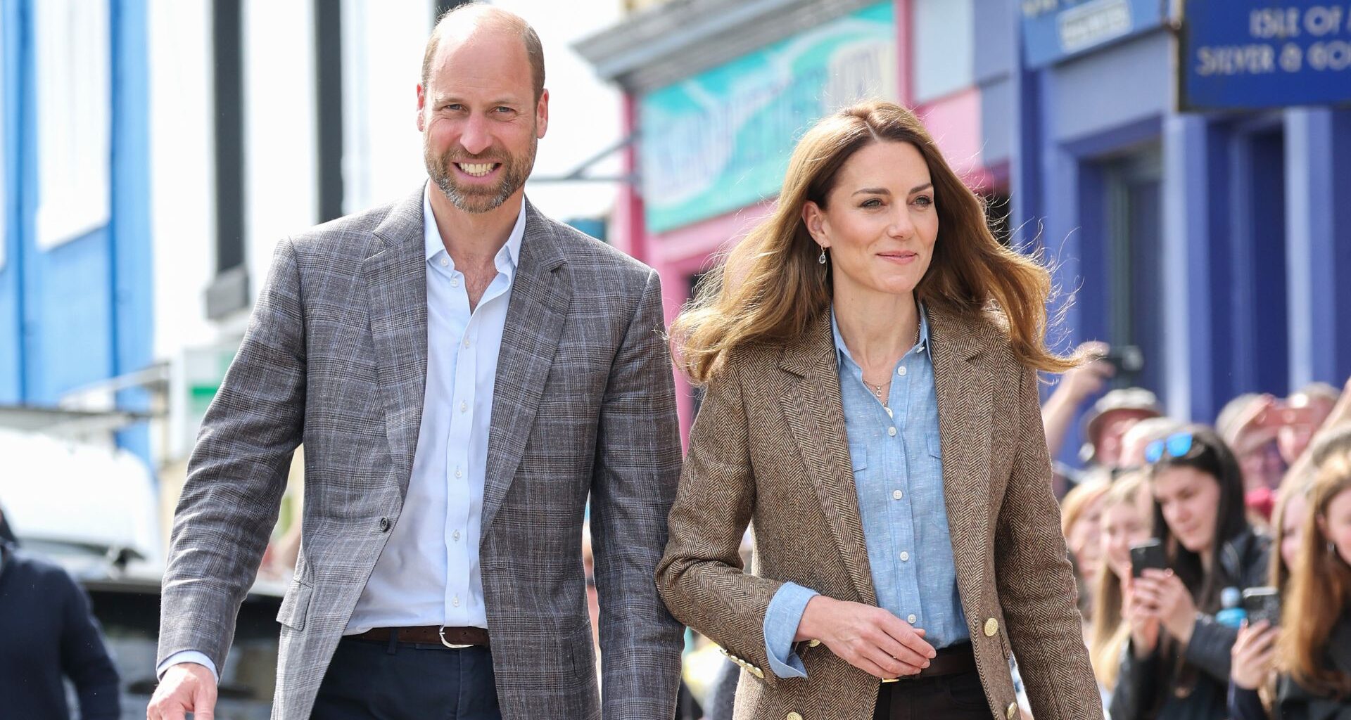 Prince William and Kate Middleton smiling as they walk past crowds