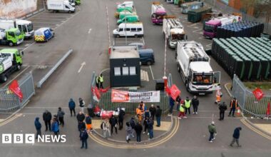 Residents hand rubbish to refuse workers at a Mobile Household Waste Centre in Senneleys Park on 8 April. One woman in a long beige cardigan is handing over two black bin bags and another in a pink coat is walking up with bags to deliver.