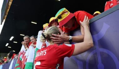 Rhiannon Roberts with her back to the camera. She is at the audience stand holding on to a woman's arm. The woman is holding on to Rhiannon's face and is consoling her while other fans to her left look on.
