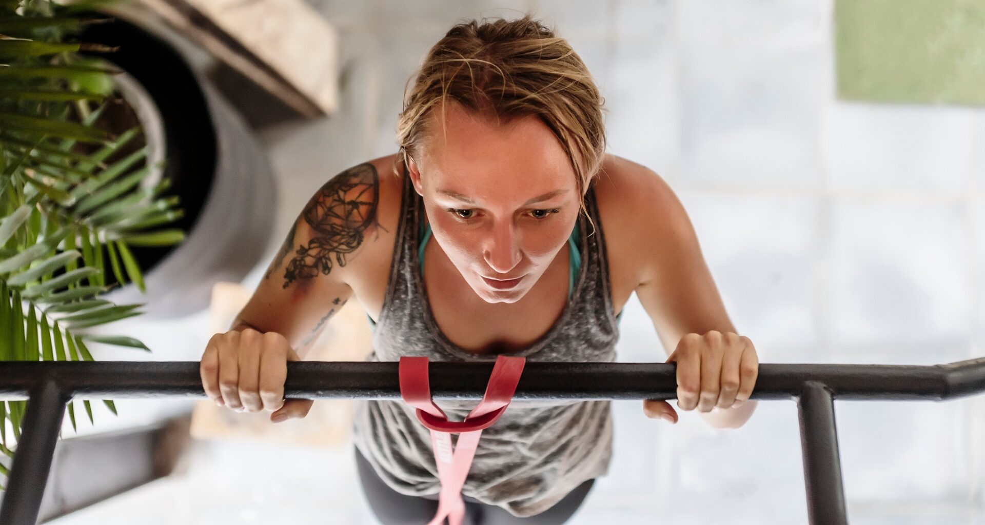 a shot from above of a woman performing a pull-up. there's a plant to the side of her and tiled floor beneath her.