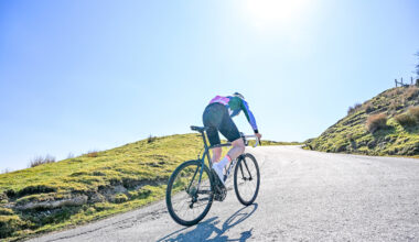 A rider climbing a hill, blue kit, blue sky, glaring sunlight, with the sun directly overhead and almost in shot